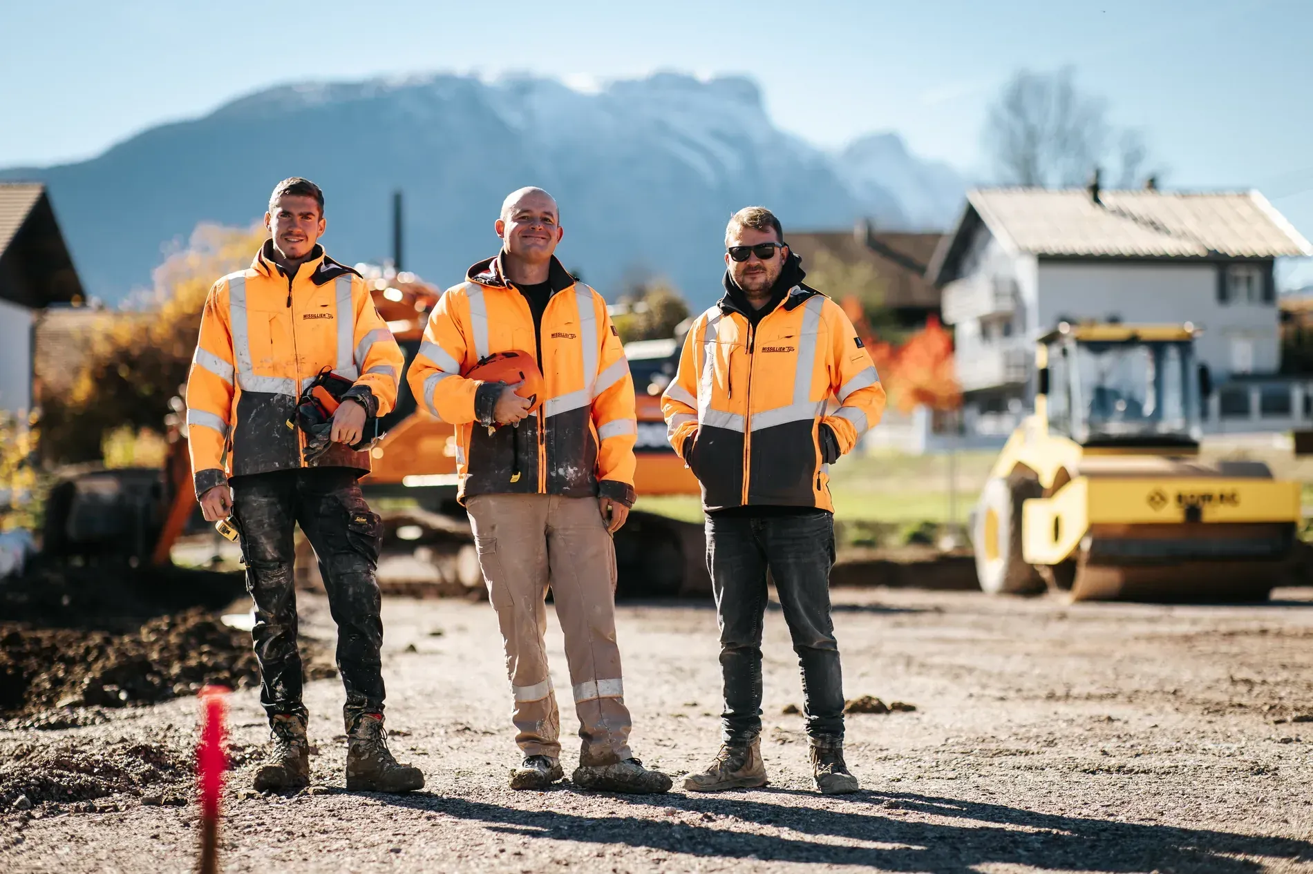 Trois compagnons du groupe MISSILLIER en tenue de chantier devant un compacteur